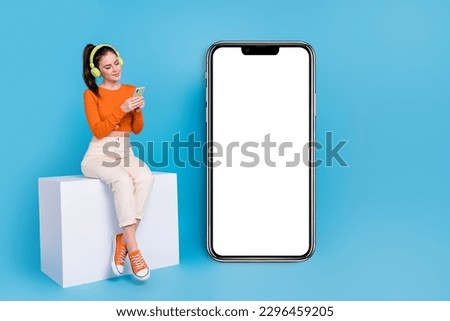 Full body photo of brown haired girl near phone promotion chatting listen music in earphones isolated on blue color background