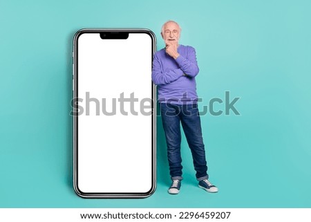 Full length photo of cheerful handsome man hand touch chin empty space big telephone screen isolated on cyan color background