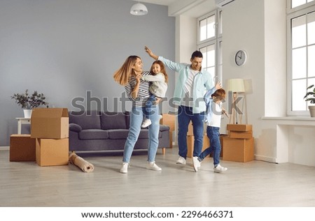 Happy family with two children are happy to move to new apartment. Young loving parents with their children dance together for joy in the living room of new house. Moving, buying or renting home. Royalty-Free Stock Photo #2296466371