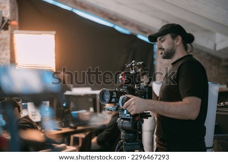 Director of photography with a camera in his hands on the set. Professional videographer at work on filming a movie, commercial or TV series. Filming process indoors, studio Royalty-Free Stock Photo #2296467293