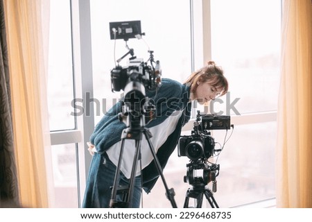 The director of photography is a woman behind a video camera on the set. A professional videographer at work on the filming of a movie, commercial or TV series. Filming process indoors, studio