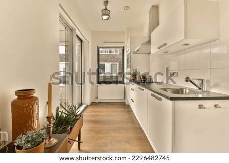 a long narrow kitchen with wood flooring and white cabinets in the center of the room is an open door that leads to a Royalty-Free Stock Photo #2296482745