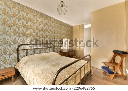 a bedroom with a bed, chair and wallpapered walls in the background is gold leaf pattern on the wall