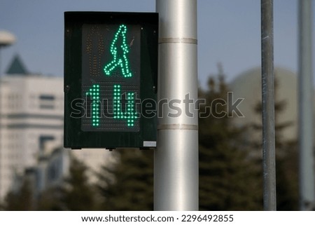 Black traffic light located within the city limits shows a green permissive signal for crosswalk traffic. The time timer shows the remaining crossing time of 14 seconds.