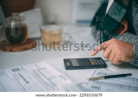 Close-up of a man's hands with a calculator and a lot of utility bills on the table. The man considers the costs of gas, electricity, heating. The concept of increasing tariffs for services
