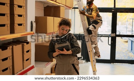 Depot manager talking on landline phone to inspect products logistics in storage room. Young supervisor discussing with headquarters about production and quality control, using tablet. Royalty-Free Stock Photo #2296534363
