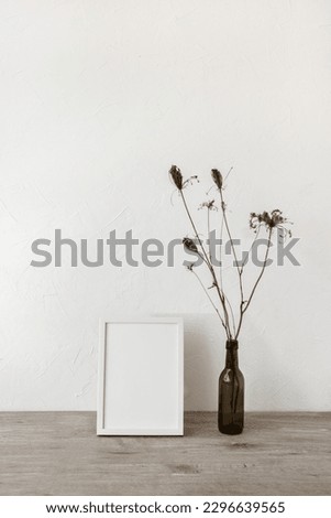 Empty picture frame and vase with flowers on a neutral beige wooden tabletop, white wall background, minimalist sustainable interior design template, copy space