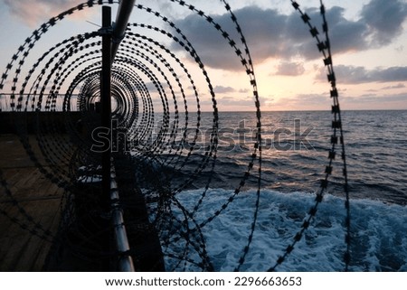 Ship prepared for transiting through piracy risk waters in Gulf of Aden, razor wire all around the ship during sunset Royalty-Free Stock Photo #2296663653