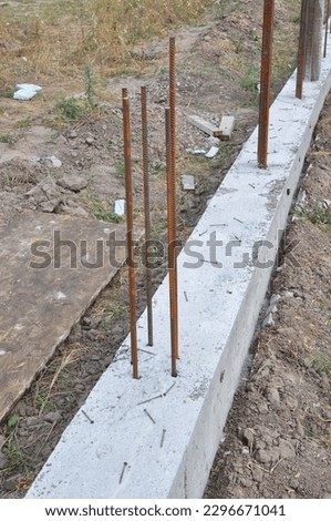 The concrete footer for new fence mounting. Fence footings. Close up on reinforced concrete footing for fence foundation with reinforcing bar. Royalty-Free Stock Photo #2296671041