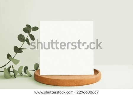 Blank Greeting Card, Invitation Mockup. Front view Eucalyptus Plant, Modern Wooden Plate, Boho Paper Mock Up on Green Table Copy Space. Minimal Business Brand Template. Soft Shadow Nordic Flier Design