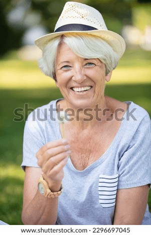 woman sitting outdoors blowing dandelion head Royalty-Free Stock Photo #2296697045