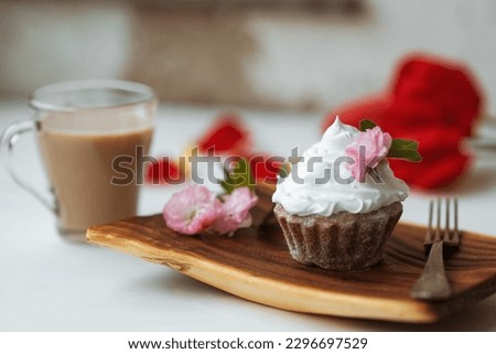 Cake and Coffee. Tasty cake with cream and pink flower decor in wooding plate. Red flowers on background. Good morning. Perfect breakfast