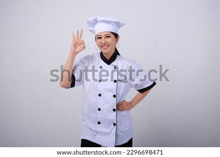 Photo of smiling female Asian chef standing showing OK hand sign gesture of approval on isolated white background