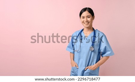 Image of young female doctor smiling and standing on the pink isolated background. Royalty-Free Stock Photo #2296718477