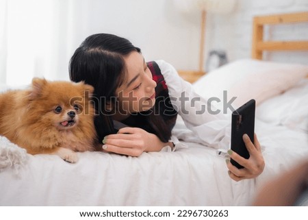 Beautiful asian woman holding a phone trying to take a picture with her furry dog ​​on the bed in the bedroom.