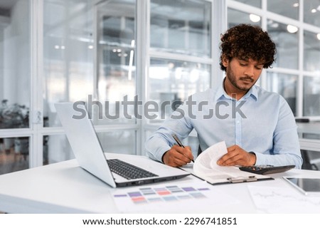 Serious and concentrated financier businessman inside office at workplace sitting at table and signing contract account documents, successful hispanic man in shirt with curly hair at work.
