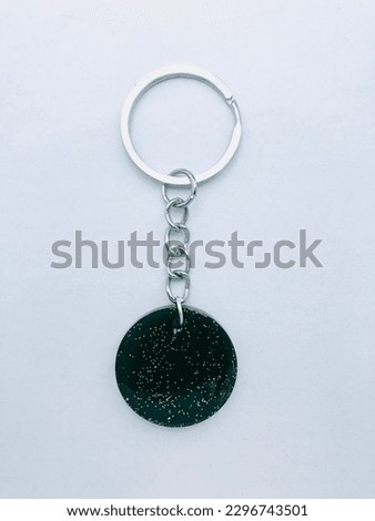 A dark green colour, circle shape keytag on a white background. The inside of the keytag has green colour glitter powder. It is made of resin material. This keytag has silver colour key chain.