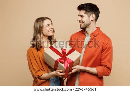 Young fun couple two friends family man woman wear casual clothes looking camera hold present box with gift ribbon bow together isolated on pastel plain light beige color background studio portrait