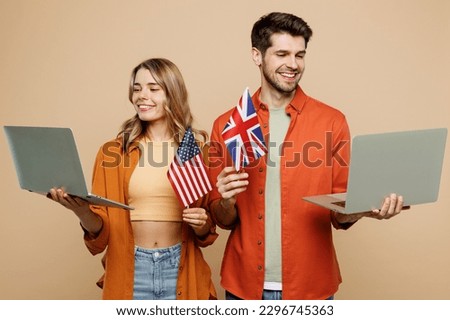 Young couple two friends family IT man woman wear casual clothes looking camera use work on laptop pc computer hold American British flag together isolated on pastel plain light beige color background Royalty-Free Stock Photo #2296745363