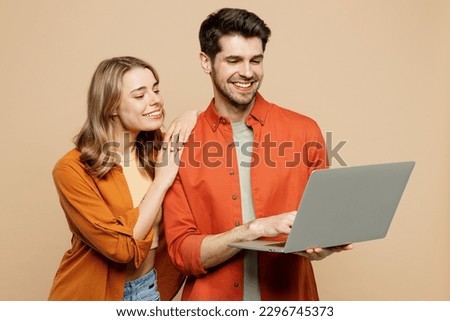 Sideways young happy couple two friends family IT man woman wearing casual clothes hold use work on laptop pc computer together isolated on pastel plain light beige color background studio portrait