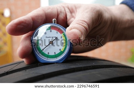 The hand of a man is measuring the tread depth of a car tire in mm. He presses a gauge into a tire tread to measure its depth. The correct depth in the tread of a tire can prevent accidents. Royalty-Free Stock Photo #2296746591