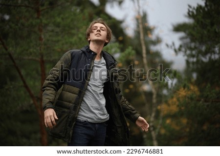 a handsome young guy with long hair in a jacket lowered his jacket, in a t-shirt.  autumn blurred background Royalty-Free Stock Photo #2296746881
