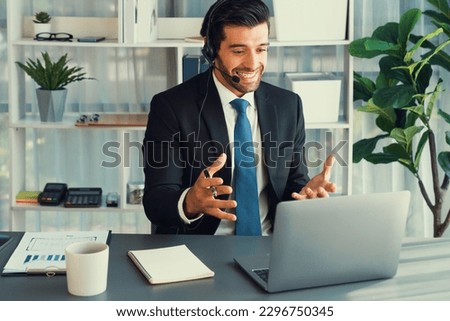 Male call center operator or telesales representative siting at his office desk wearing headset and in conversation with client providing customer service support or making persuasive sale. fervent Royalty-Free Stock Photo #2296750345