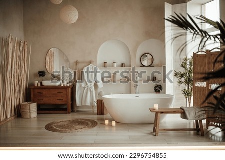 Soft native hues organic shapes look of bathroom with big window oval bathtub in neutrals tones. Green palm plants candles bubblebath leasure and relaxation skin selfcare wellness luxury living Royalty-Free Stock Photo #2296754855