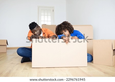 Upset Black Spouses Leaning At Cardboard Box, Feeling Tired While Moving To Their New Home, Exhausted African American Couple Suffering Stress During Relocation, Feeling Depressed, Copy Space