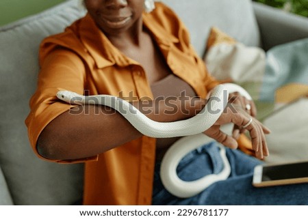 Close-up of white rat snake creeping over arms of young African American female owner holding exotic pet during animal assisted therapy