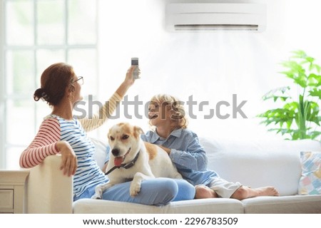 Mother and child with air conditioner remote control. Comfortable temperature at family home. Cooling and heating device. Mom and kid on couch under cold breeze. Air conditioning on hot summer day.  Royalty-Free Stock Photo #2296783509