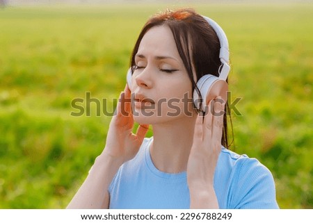 A woman  in listening to music in headphones, closing her eyes as Outside, surrounded by nature,deep relaxation, embracing the tranquility of the moment. Royalty-Free Stock Photo #2296788249