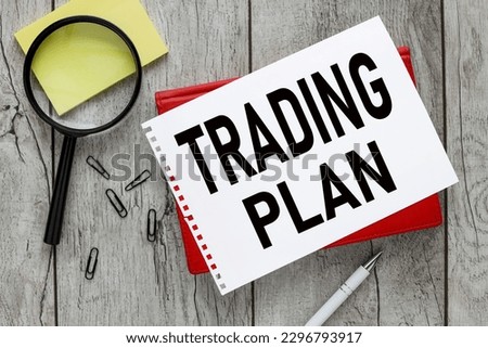 Trading plan. magnifier and yellow sticker. text on white paper on a red notepad. Royalty-Free Stock Photo #2296793917
