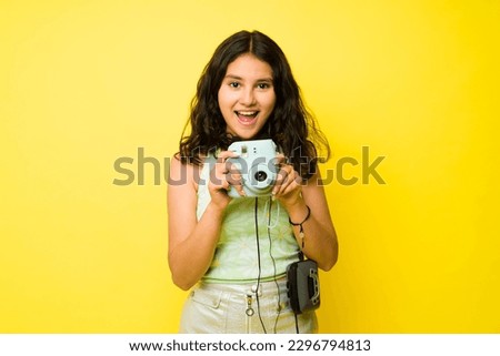 Portrait of an excited thirteen-year-old girl laughing having fun while taking pictures using her instant camera