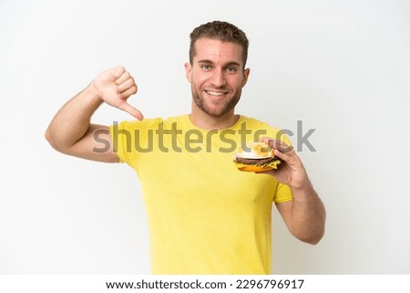 Young caucasian man holding a burger isolated on white background proud and self-satisfied