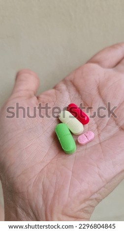 Medicine capsules or pills of various colors over palms. 