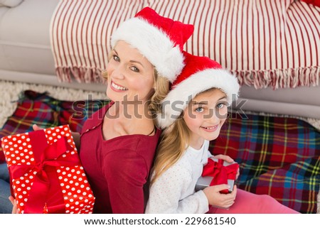 Festive mother and daughter smiling at camera with gifts at home in the living room