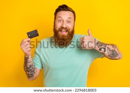 Photo of positive glad man wear trendy clothes recommend debit card nfc payment thumb up isolated on yellow color background