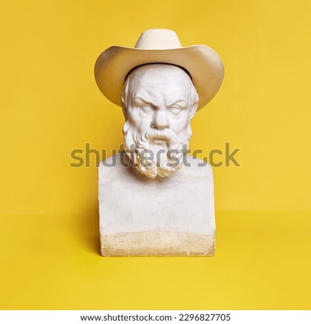 Antique statue bust of serious bearded man wearing fedora hat against yellow background. Concept of creativity, modernity and vintage, antique art. Inspiration and imagination