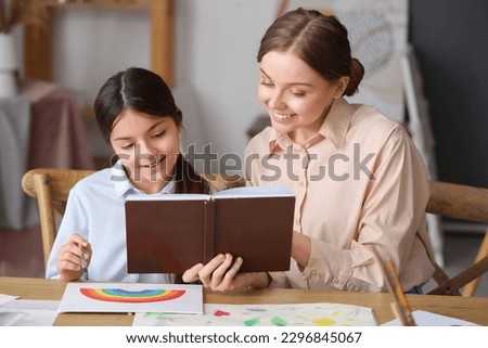 Drawing teacher with book giving private art lesson to little girl in workshop