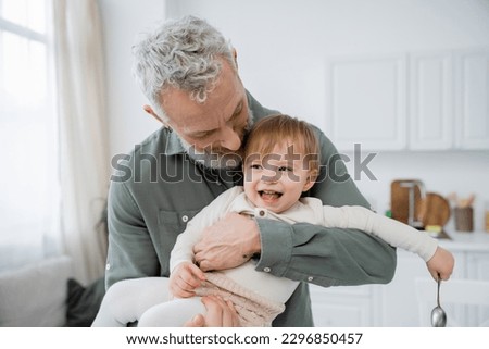 bearded mature man embracing carefree granddaughter holding spoon in kitchen Royalty-Free Stock Photo #2296850457