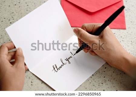 A woman hands writing a Thank You note on a greeting card with red envelope Royalty-Free Stock Photo #2296850965