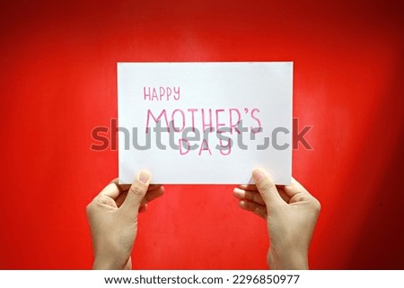 Hands holding a beautiful card with Happy Mother's Day message on a blur red background