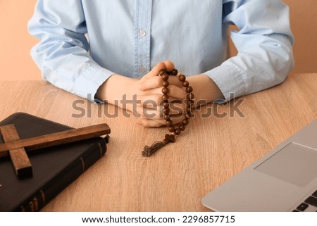 Woman with prayer beads at table on beige background, closeup