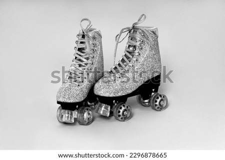 Pair of glitter silver stylish roller skates on gray background. Black and white photo.