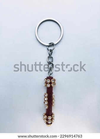 A dark red colour, cylindrical shape keytag on a white background. It is made of resin material. The top and bottom of the keytag has gold colour rows of dots. This keytag has silver colour keychain.