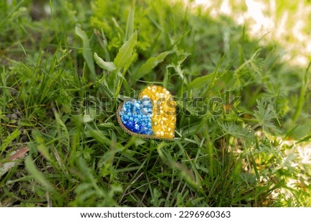 brooch in the form of a yellow-blue heart on a background of grass. colors of the flag of Ukraine, yellow-blue heart