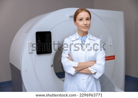 Young adult blonde doctor standing near computed tomography scanner in a hospital, wearing lab coat.