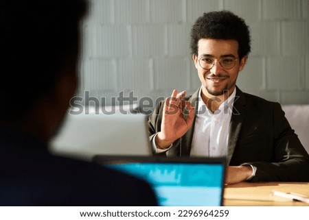 Young smilling businessman showing okay sign to his colleague or applicant with laptop sitting in front of him during communication