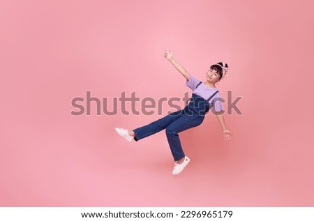 smiling asian girl floating in mid-air and pointing finger isolated on pink studio background. Royalty-Free Stock Photo #2296965179
